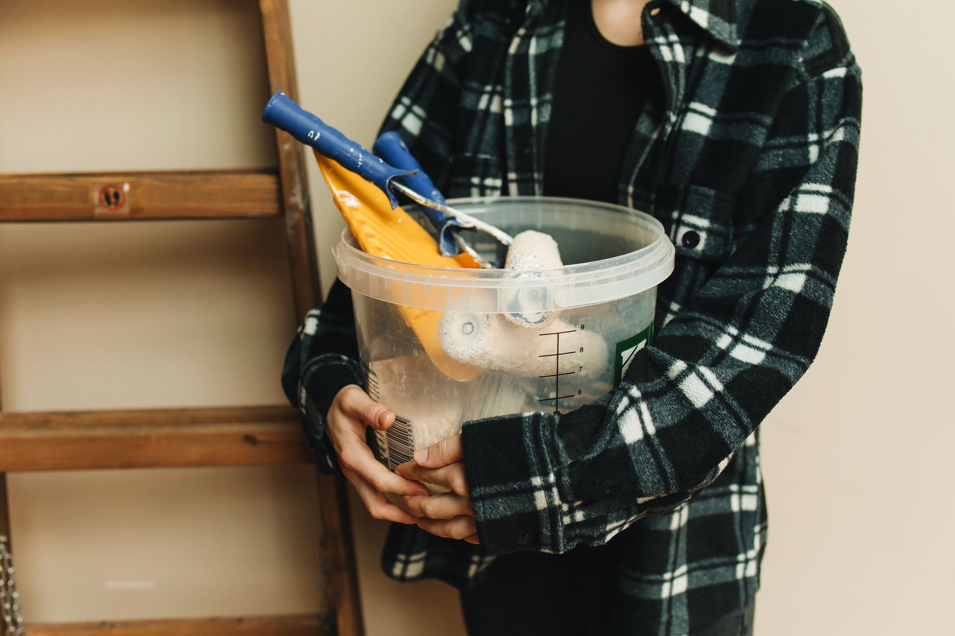 Close-up of a person holding a bucket filled with renovation tools, including paint rollers and scrapers in Long Beach, CA